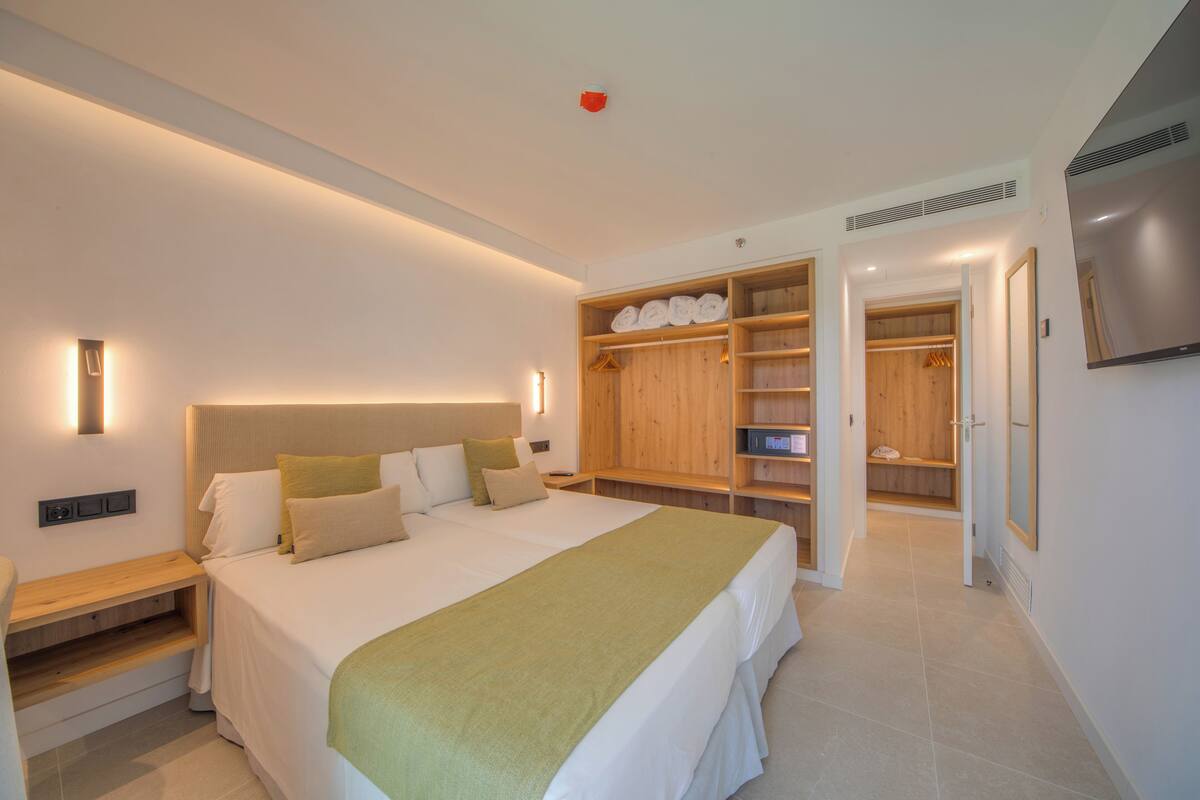 A modern hotel room with a large bed, a wooden wardrobe, a TV, and a bedside table.