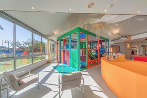 Un espacio de juego interior luminoso y moderno con estructuras coloridas y un panel de vidrio.