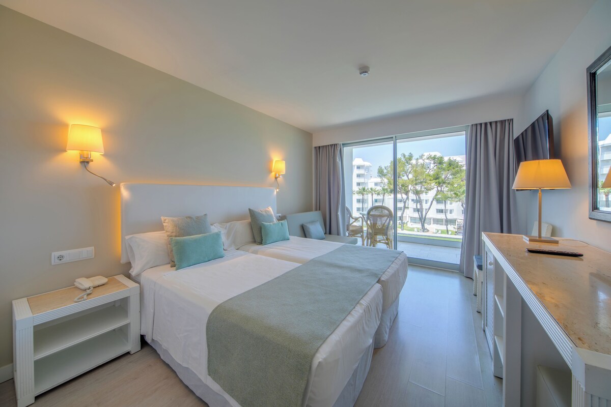 A hotel room with two beds, a desk, a chair, and a view of the outside.