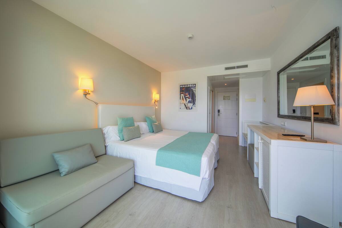 A hotel room with a bed, a sofa, a desk, and a mirror.