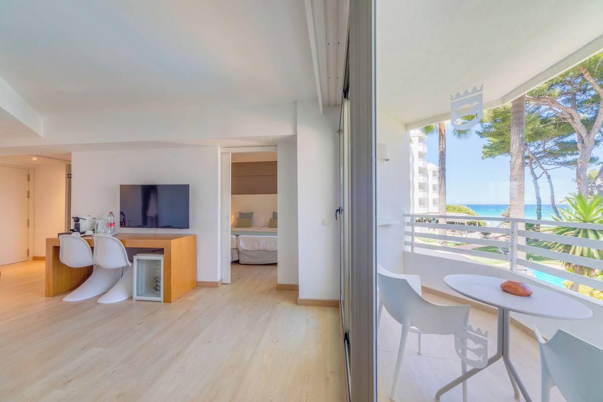 A modern hotel room with a balcony, a dining area, and a TV.