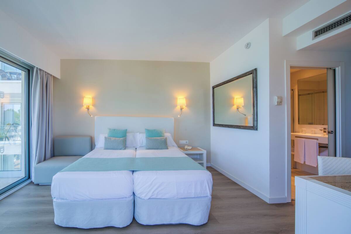 A hotel room with a large bed, bedside lamps, a mirror, and a view of the outside.