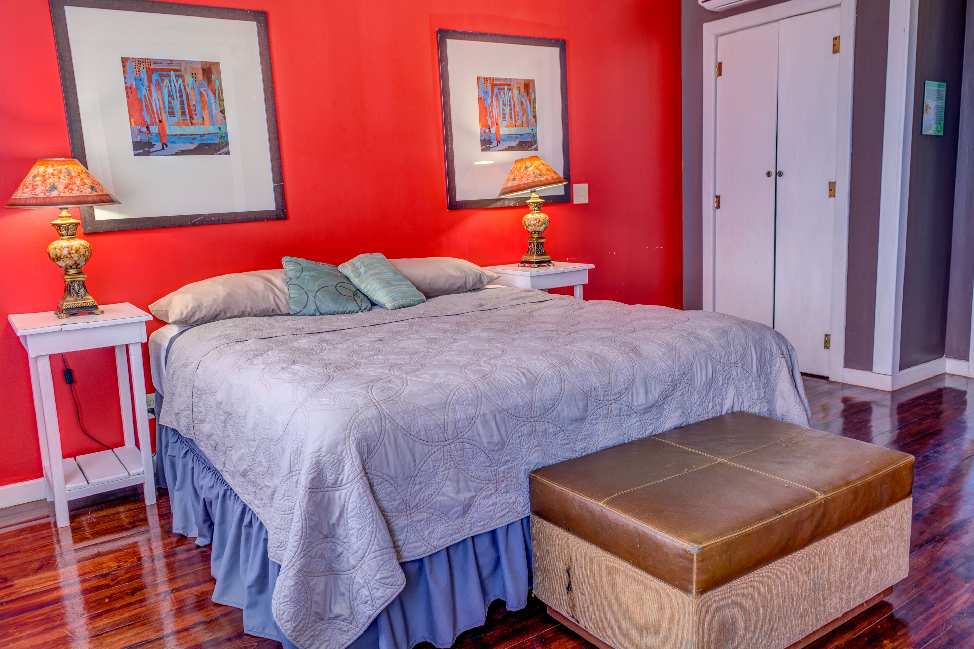 Une chambre à coucher avec un grand lit, deux tables de chevet avec des lampes, un banc et deux tableaux encadrés accrochés au mur.