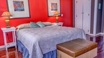 A bedroom with a large bed, two bedside tables with lamps, a bench, and two framed pictures on the wall.