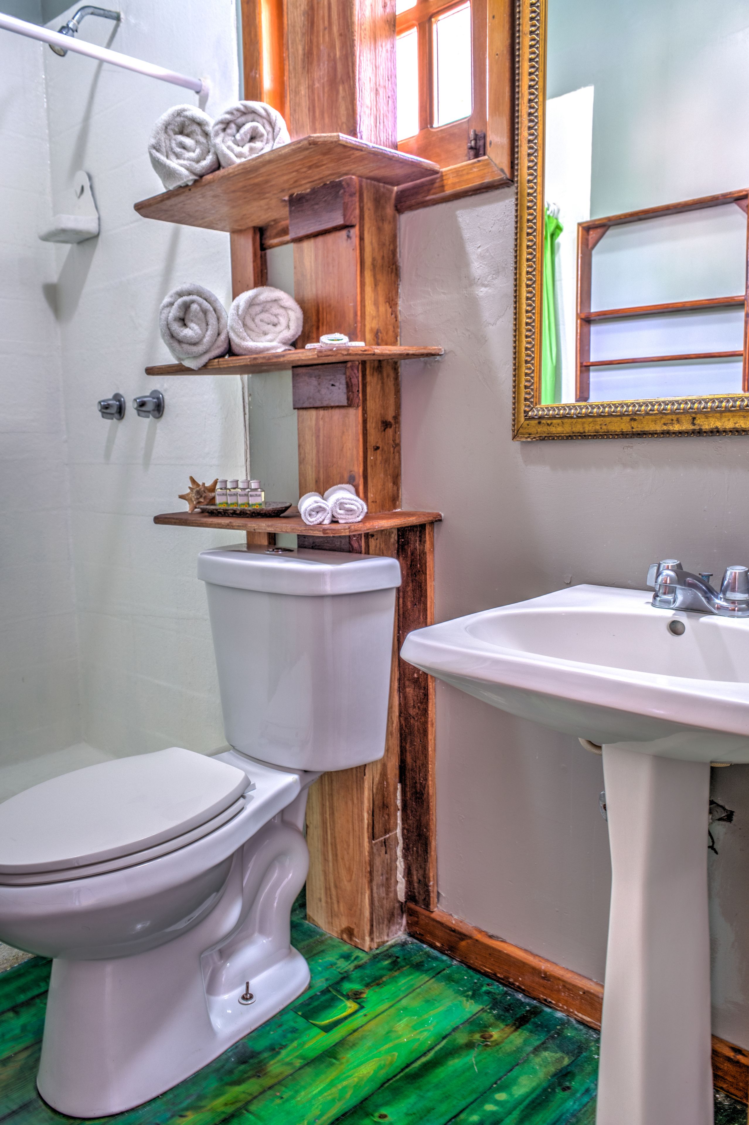 A bathroom with a toilet, a sink, and wooden shelves holding towels.