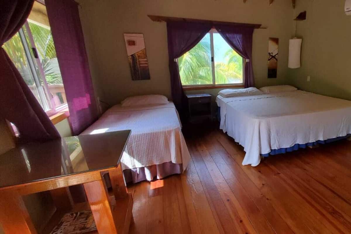 A room with two beds, wooden flooring, a desk, and a window with curtains.