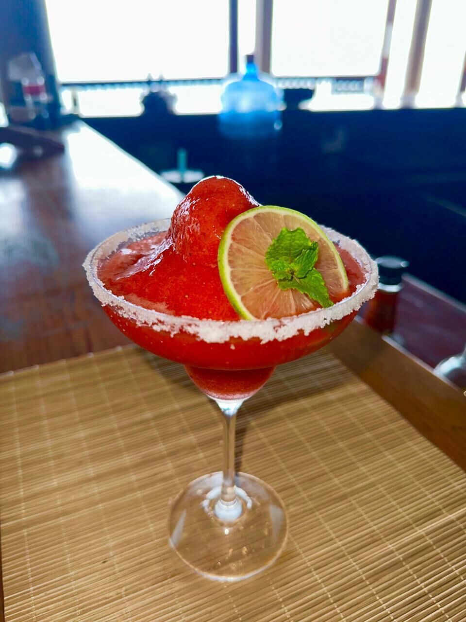 A cocktail in a glass with a salted rim, garnished with a slice of lime and mint.