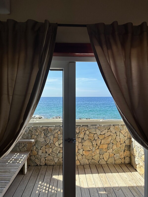 A balcony with stone walls and wooden flooring, overlooking a beach and ocean.