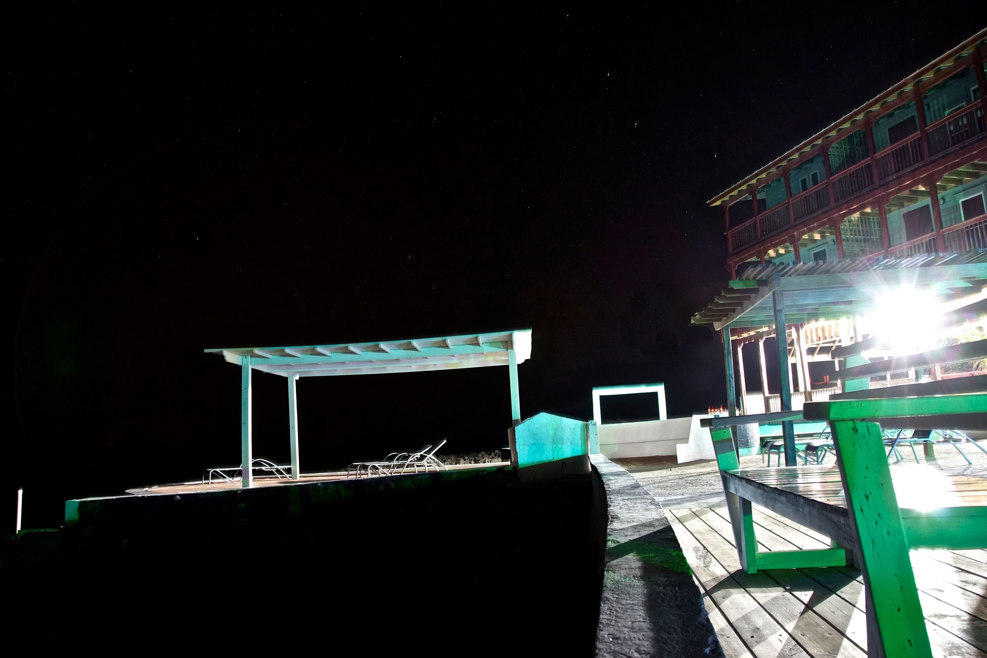 A nighttime view of a wooden deck with a covered seating area and a building with balconies in the background.