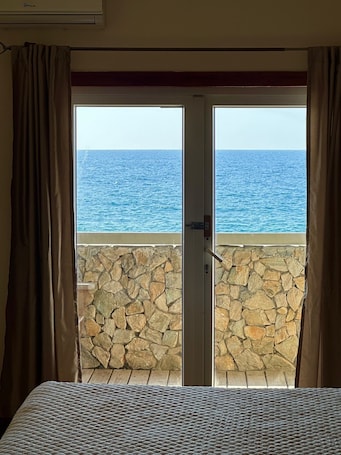 A room with a bed, a stone wall, and a view of the sea through a door.