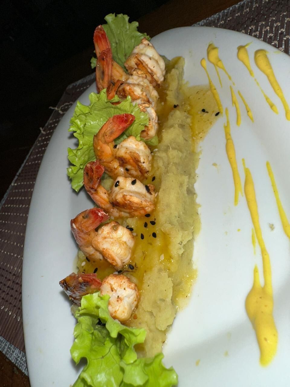 Un plato con camarones a la parrilla, lechuga y salsa amarilla.