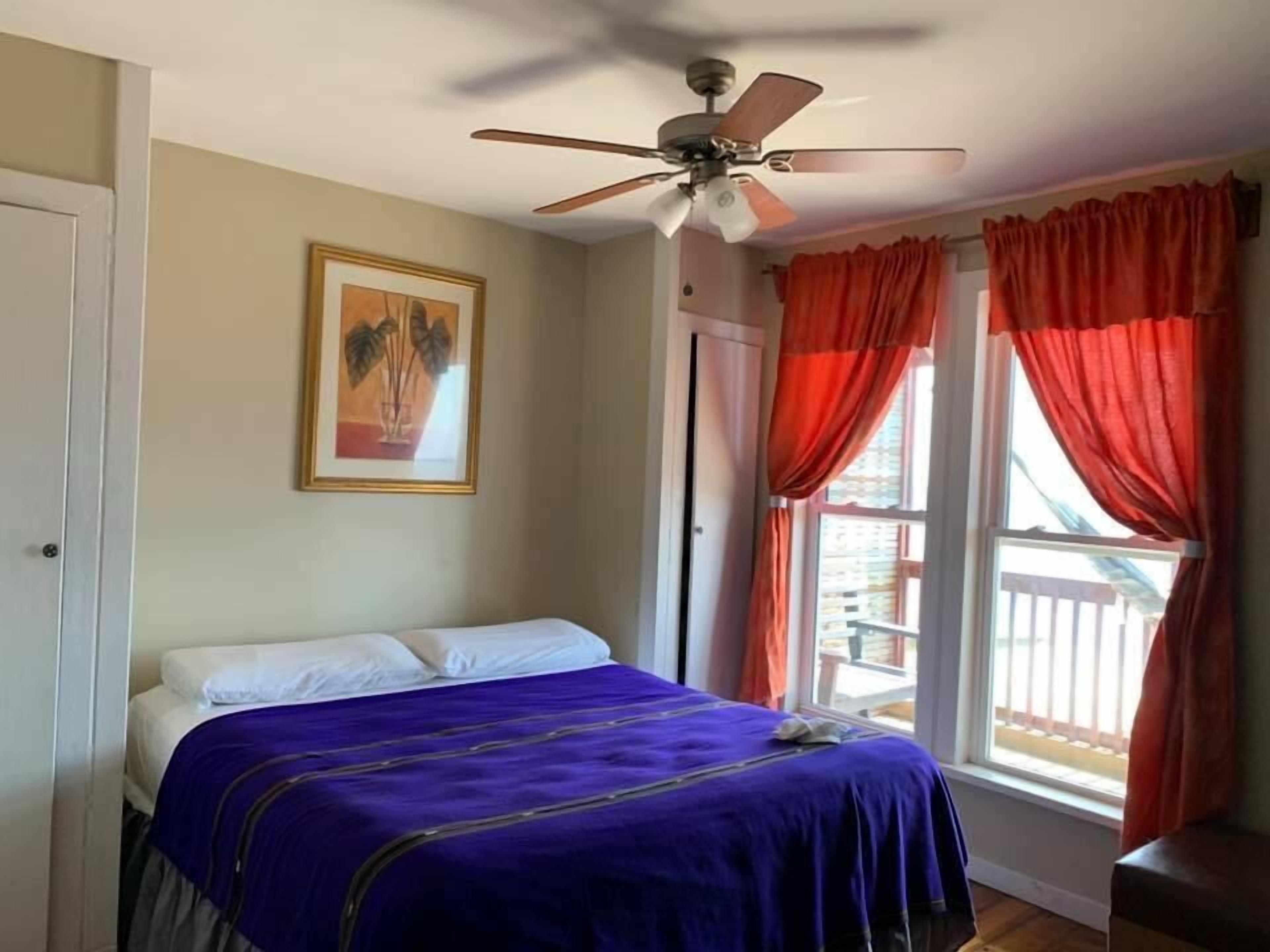 A bedroom with a bed, a ceiling fan, a window with curtains, and a framed picture on the wall.