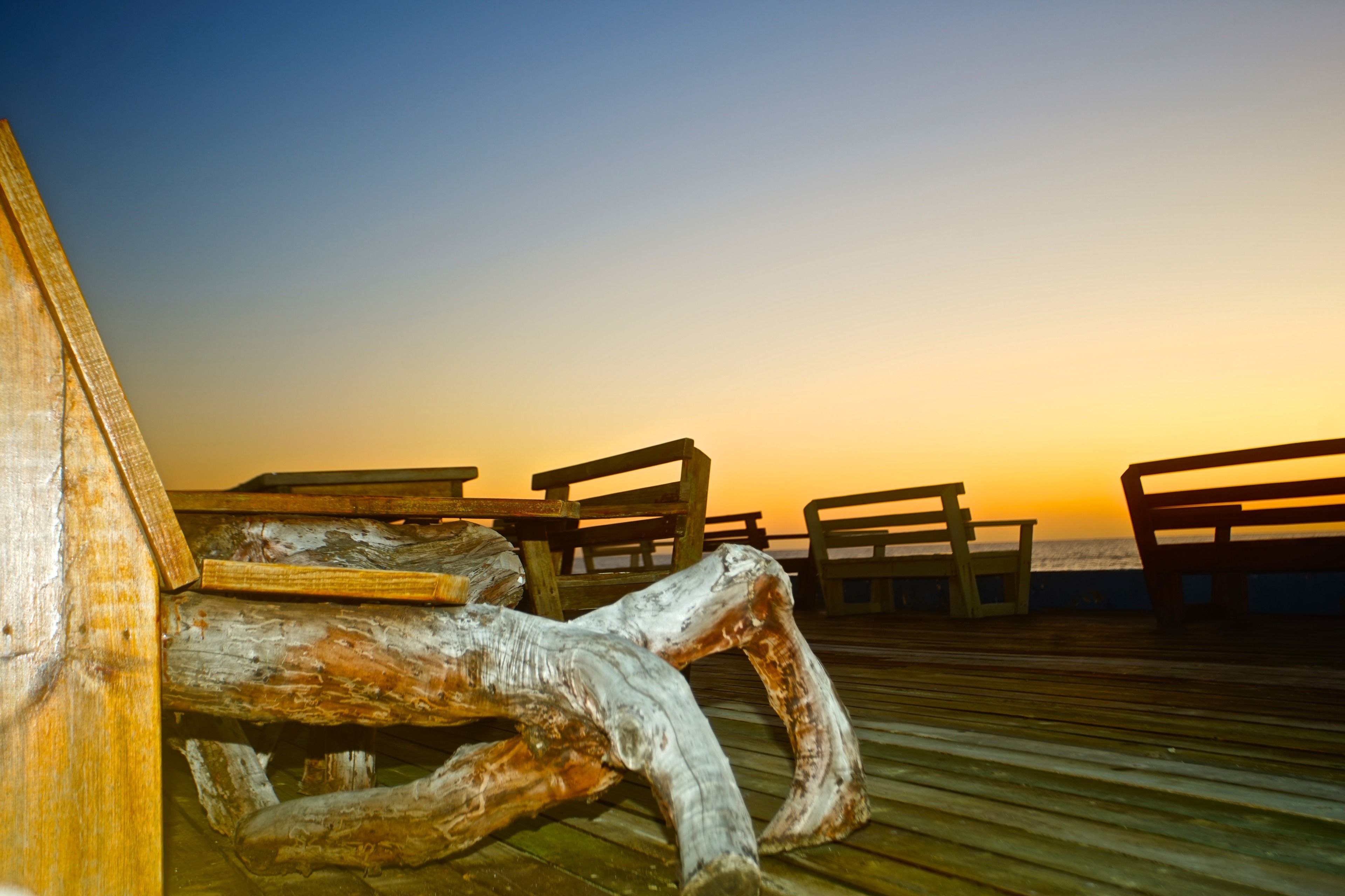 A wooden pier with benches, overlooking a sunset over the water.