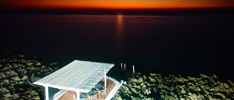 Un muelle de madera se extiende sobre aguas tranquilas de noche, bajo un cielo despejado con una luna visible.
