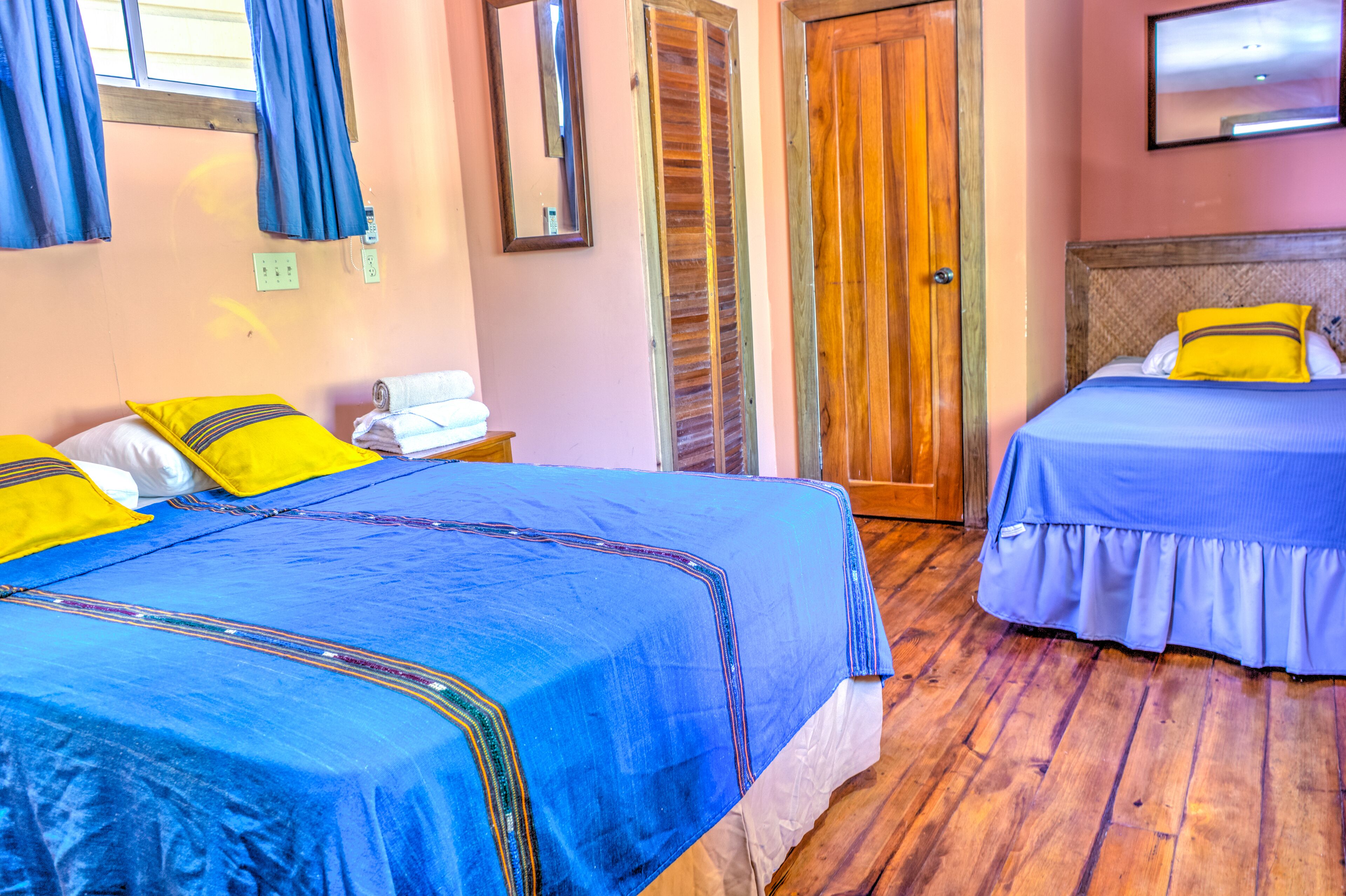 Habitación de hotel con dos camas, suelo de madera, una puerta de madera y un espejo en la pared.