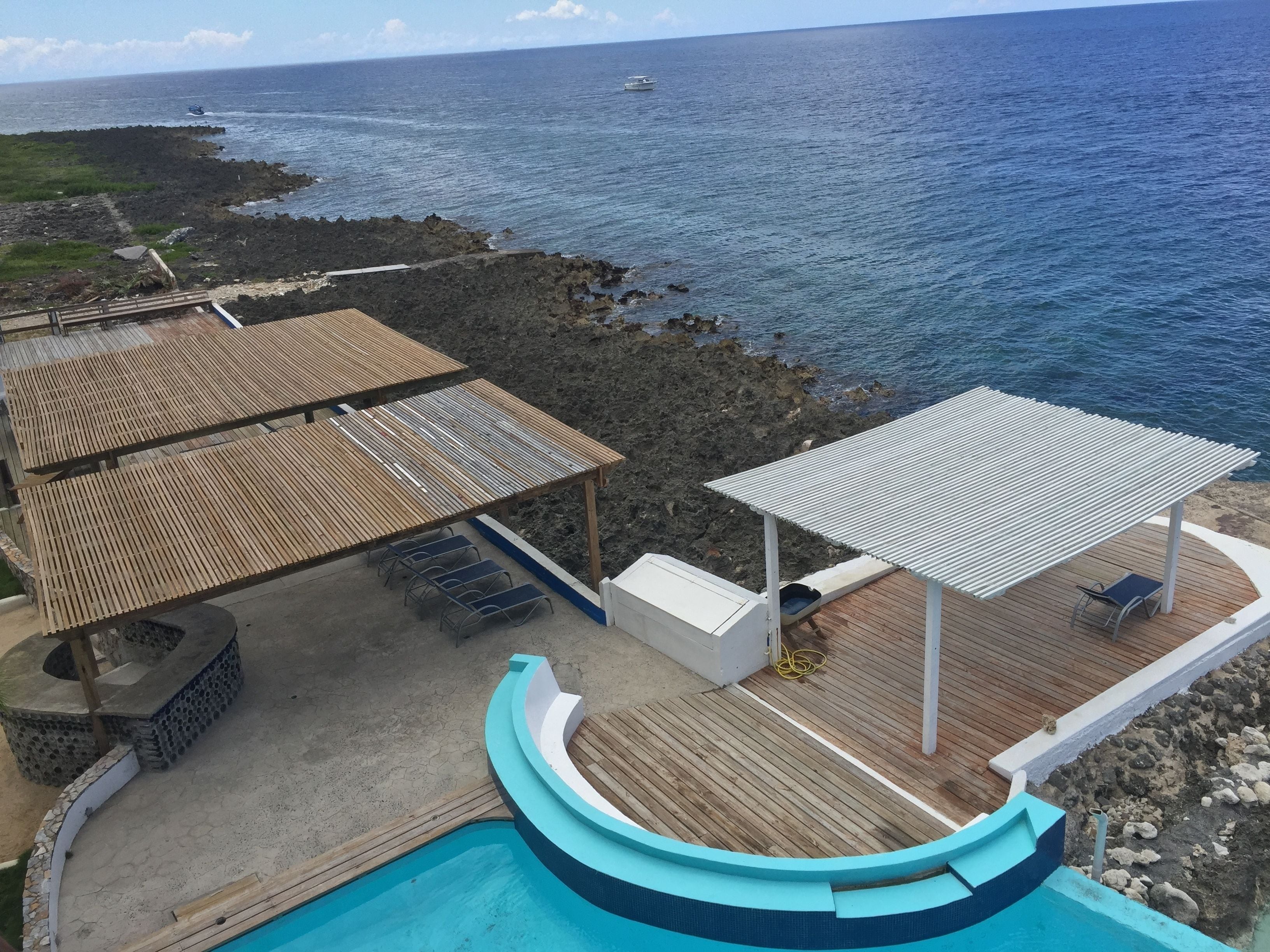 A pool area with a wooden deck and a covered seating area overlooking the ocean.