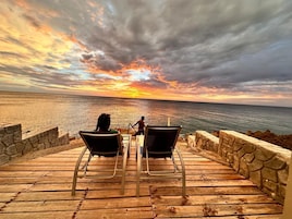 Um deck de madeira com duas cadeiras de descanso voltadas para a praia, com vista para o oceano.