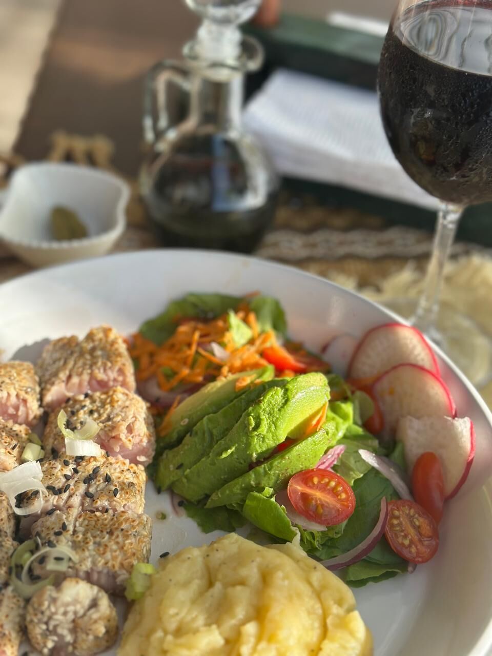Un plato de comida con una copa de vino tinto, un cuenco pequeño y una jarrón sobre una mesa.