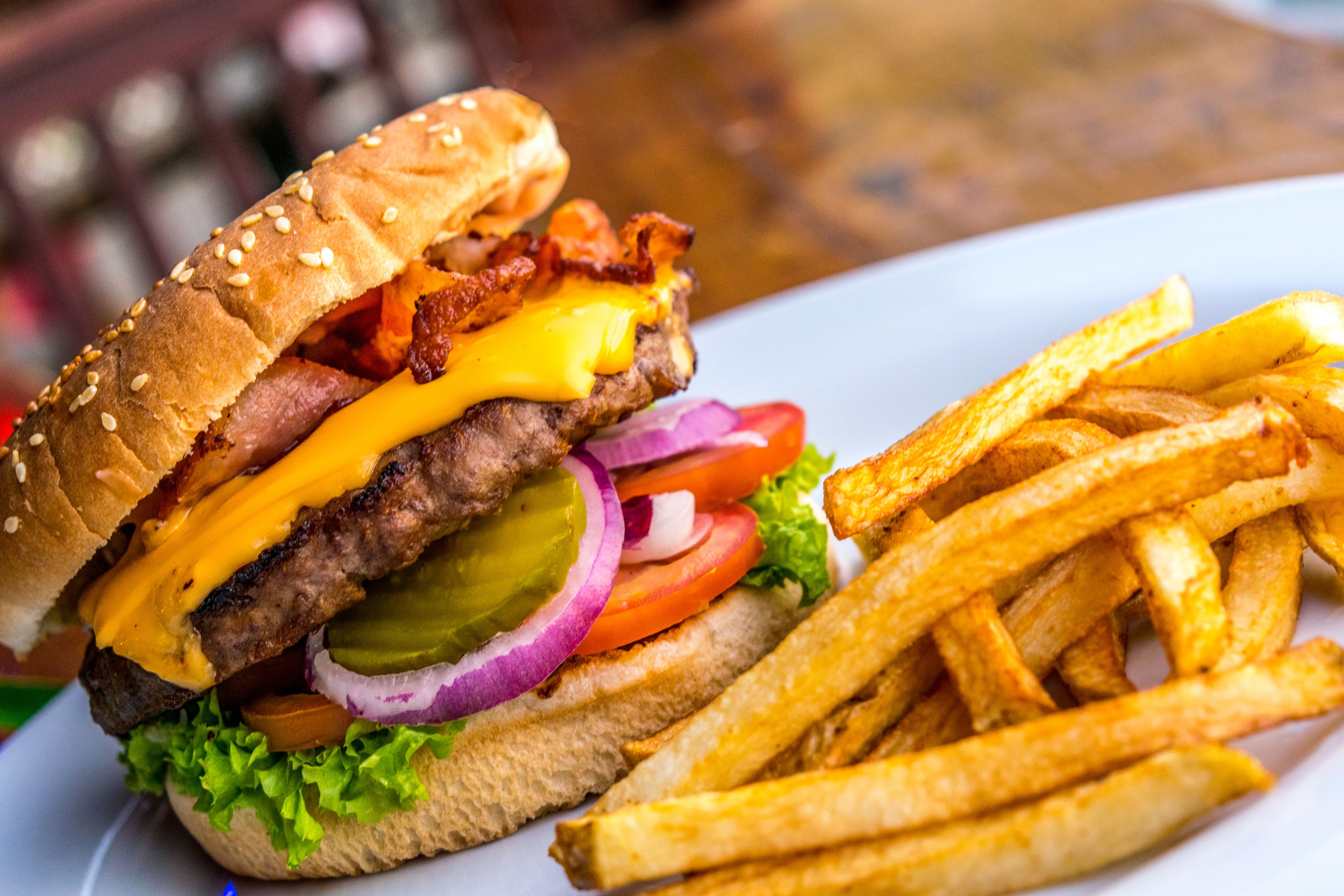 Un hamburger garni de bacon, de fromage, de laitue, de tomate et de cornichons, servi dans un pain à graines de sésame, accompagné d’une portion de frites.