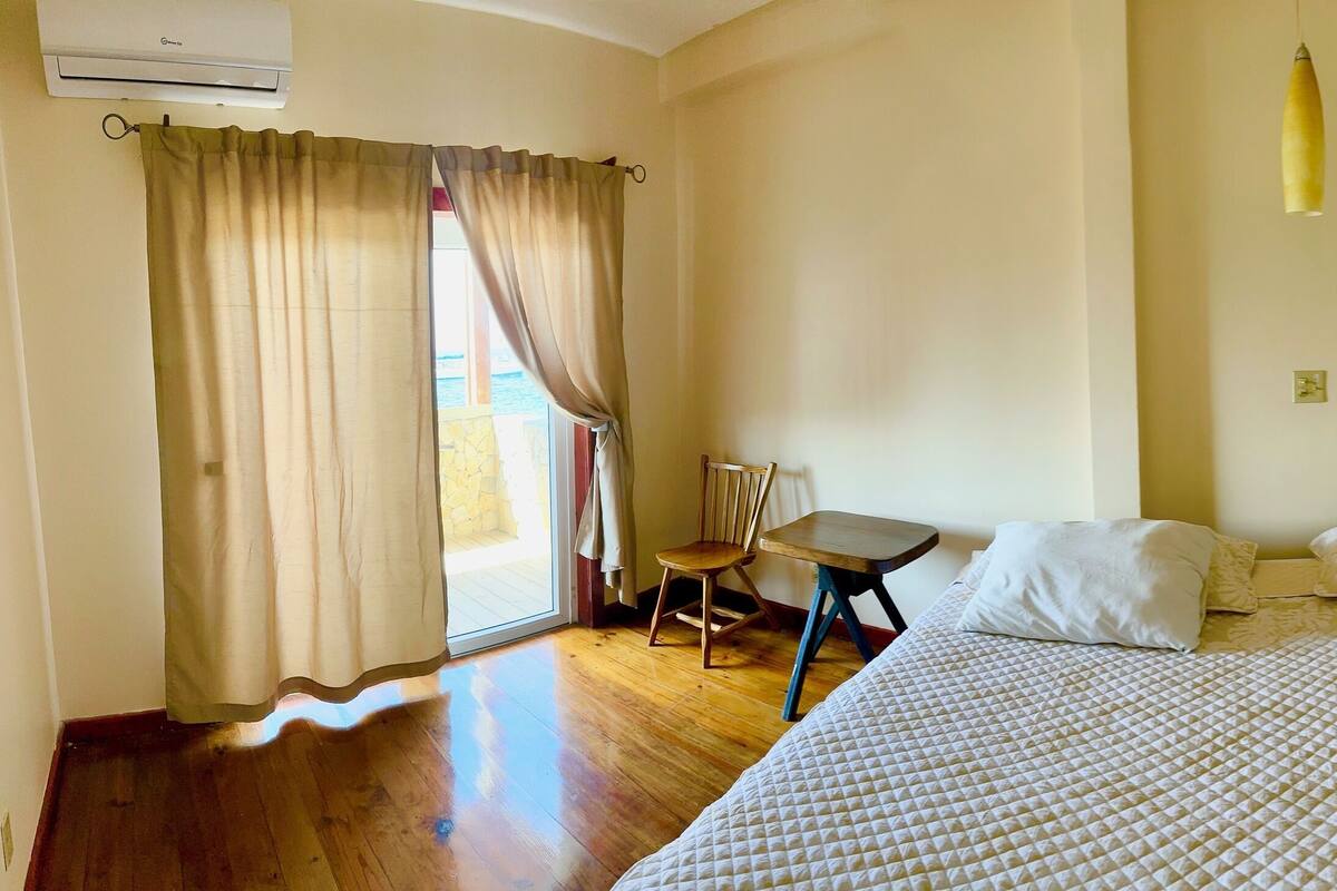 A bedroom with a large bed, a chair, a small table, and a painting on the wall.