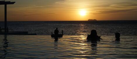 Un coucher de soleil sur une mer calme, avec trois personnes dans l’eau.