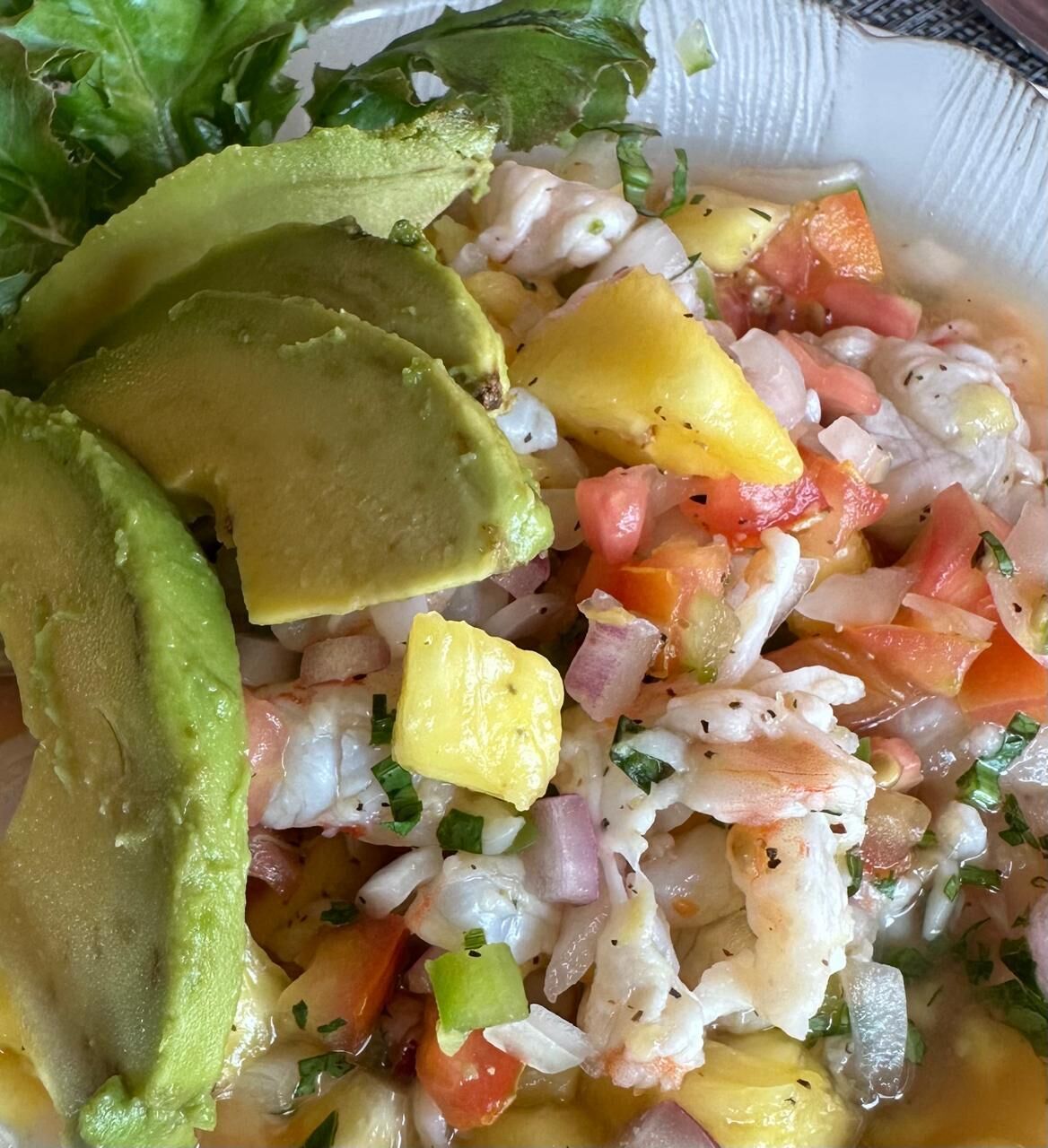 A bowl of seafood salad with avocado slices and a side of lettuce.