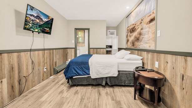 Quarto de hotel com cama, mesa de cabeceira, televisão na parede e uma janela grande.