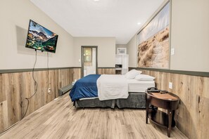 Habitación de hotel con cama, mesita de noche, televisor montado en la pared y un amplio ventanal.