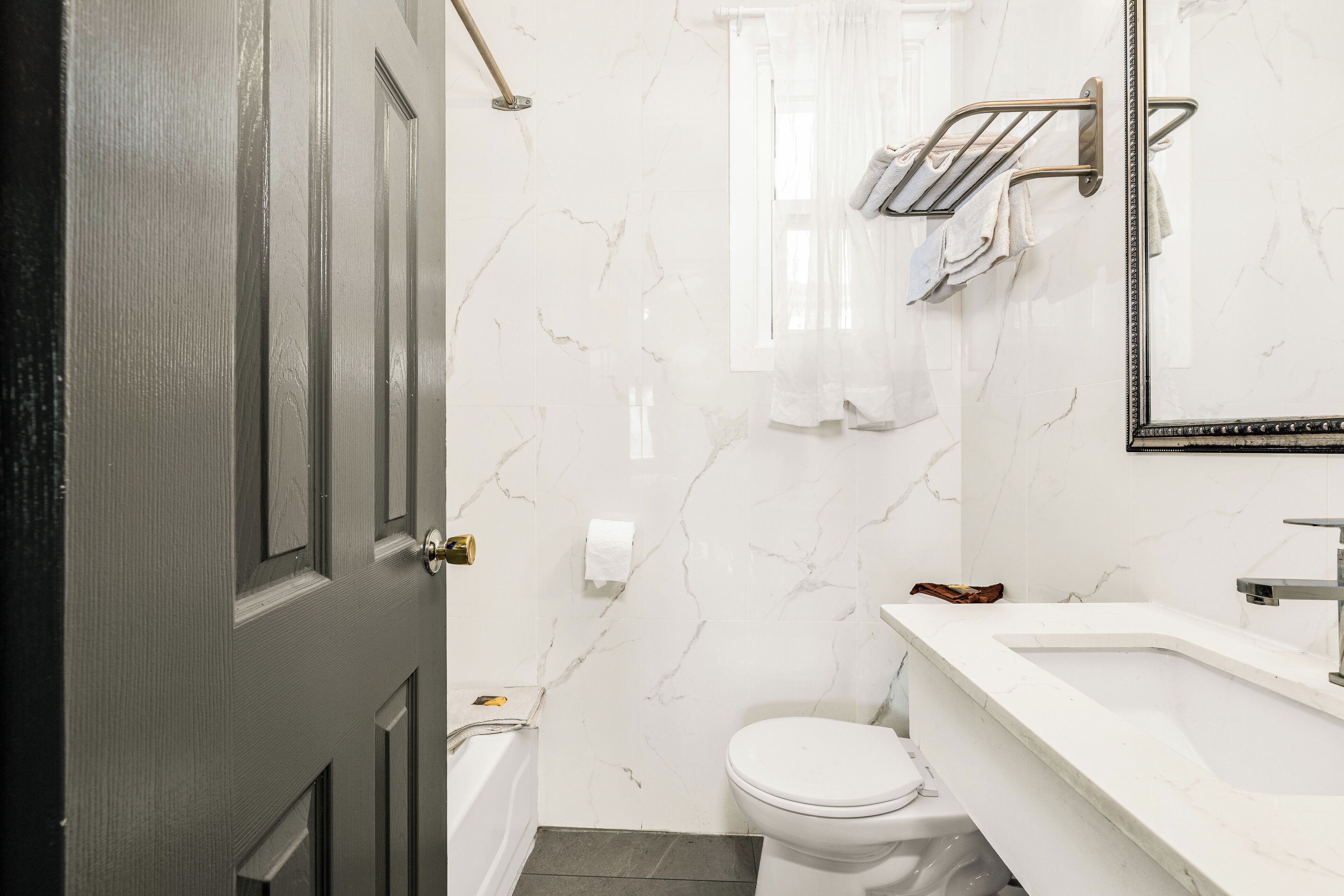 Un baño con pared de mármol blanco, un inodoro blanco, un lavabo blanco y un perchero para toallas.