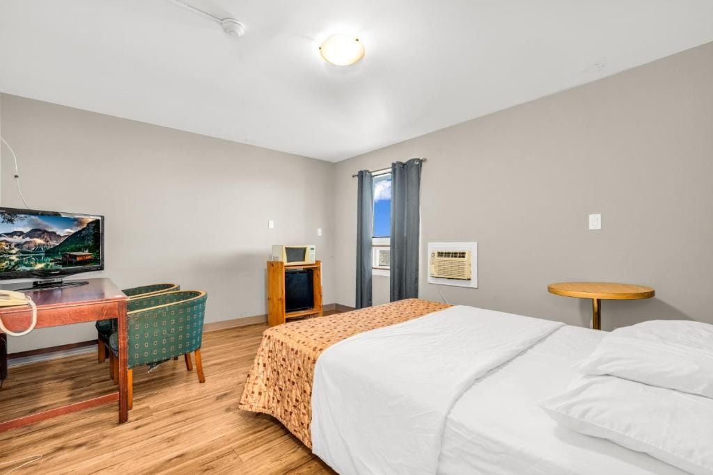 A hotel room with a bed, a desk with a television, a small table, and a window with curtains.