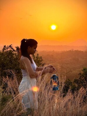 Una persona sentada en una colina con un farol, contemplando un paisaje al atardecer.