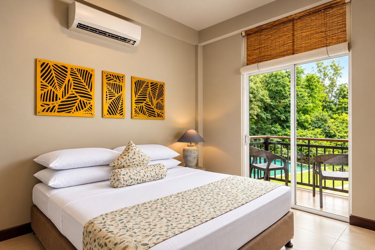 Una habitación de hotel con una cama, un ventanal con vistas a la vegetación y un balcón con mobiliario exterior.