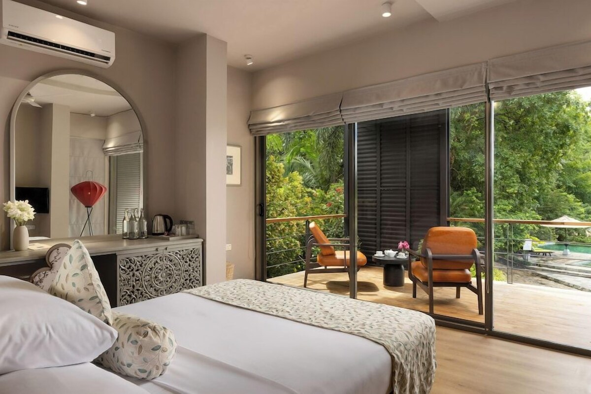 A bedroom with a large bed, a dresser, and a mirror. There is a balcony with chairs and a table.