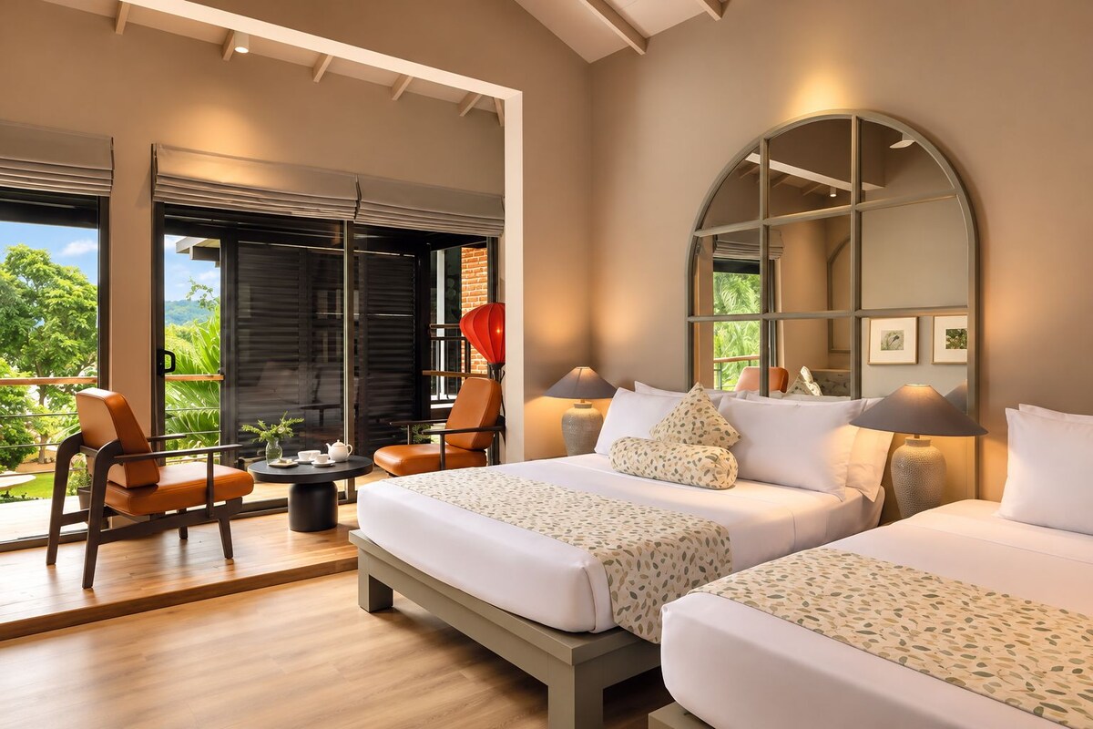Habitación de hotel con una cama grande, una zona de estar con sillas, una mesa redonda y vistas a zonas verdes.