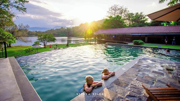 Un espace piscine avec vue sur un lac et des montagnes, un coin salon couvert et une terrasse en pierre.