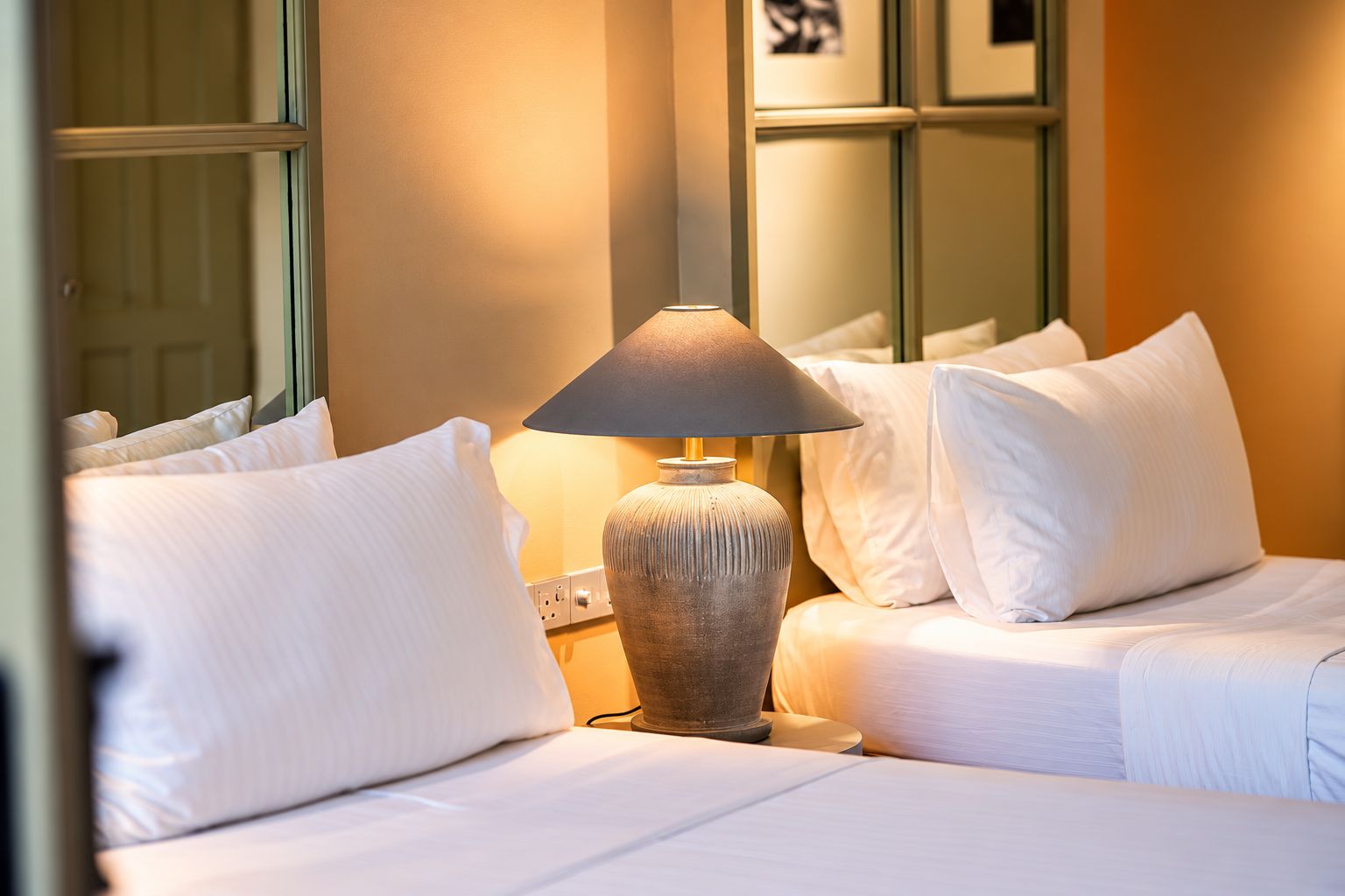 A hotel room with a bed, a lamp, and a wall with framed pictures.