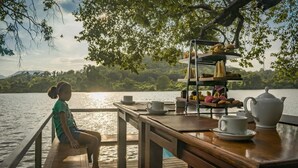 Une terrasse en bois avec un service à thé à plusieurs niveaux, une théière et une tasse posés sur une table donnant sur un lac.