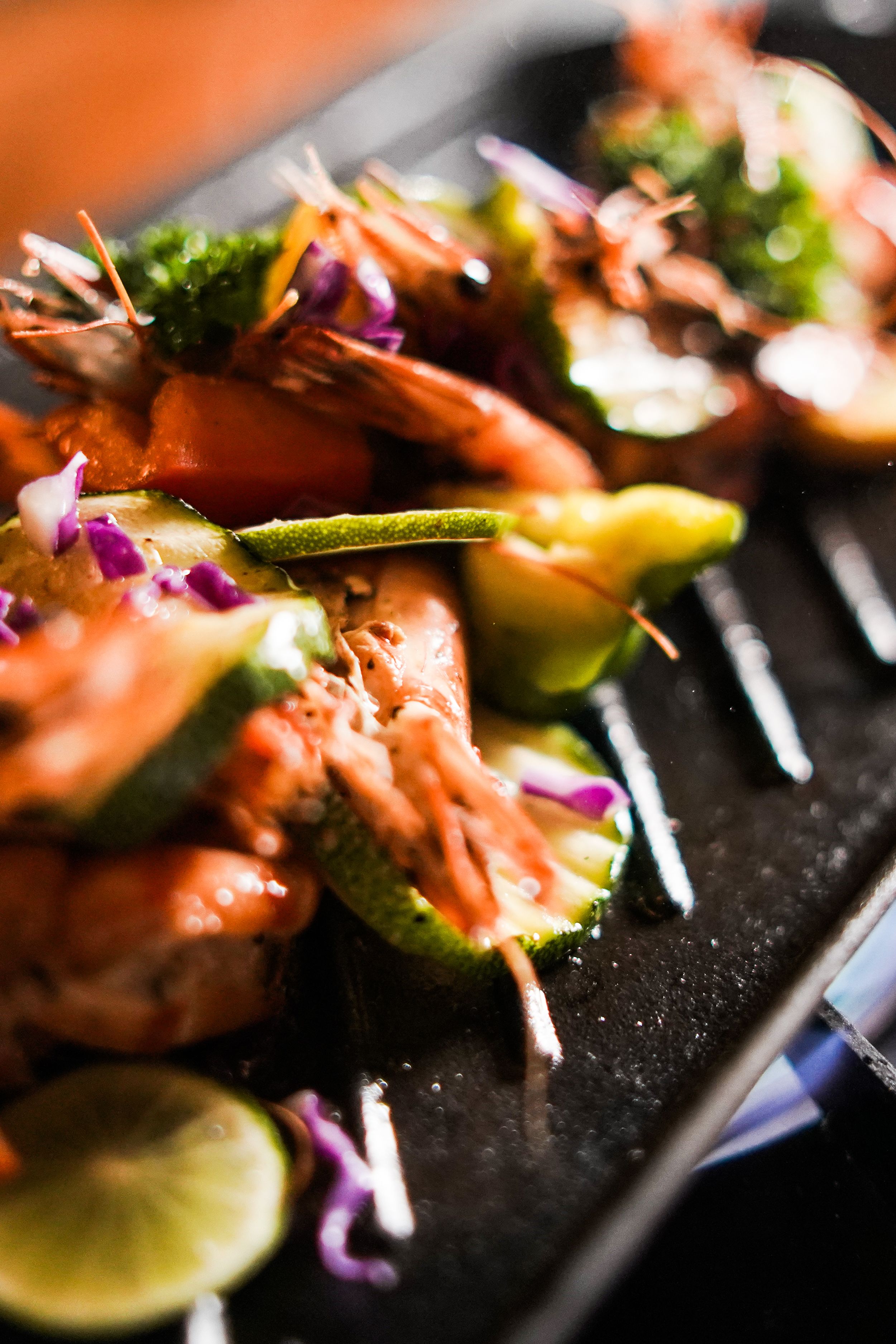 A close-up of a dish with grilled shrimp, zucchini, and lime slices.