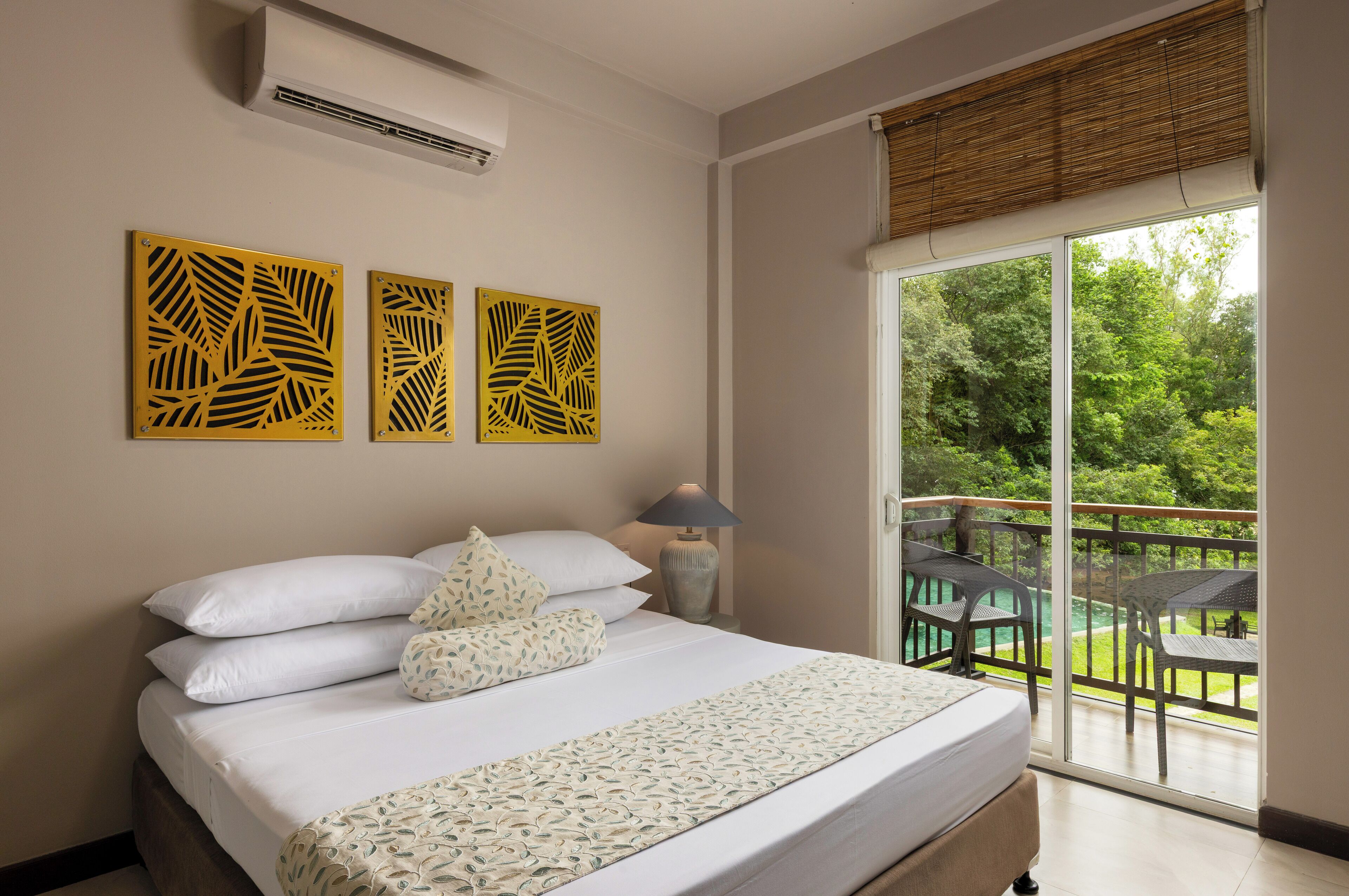 Habitación de hotel con cama, mesita de noche con lámpara y balcón con mobiliario exterior.