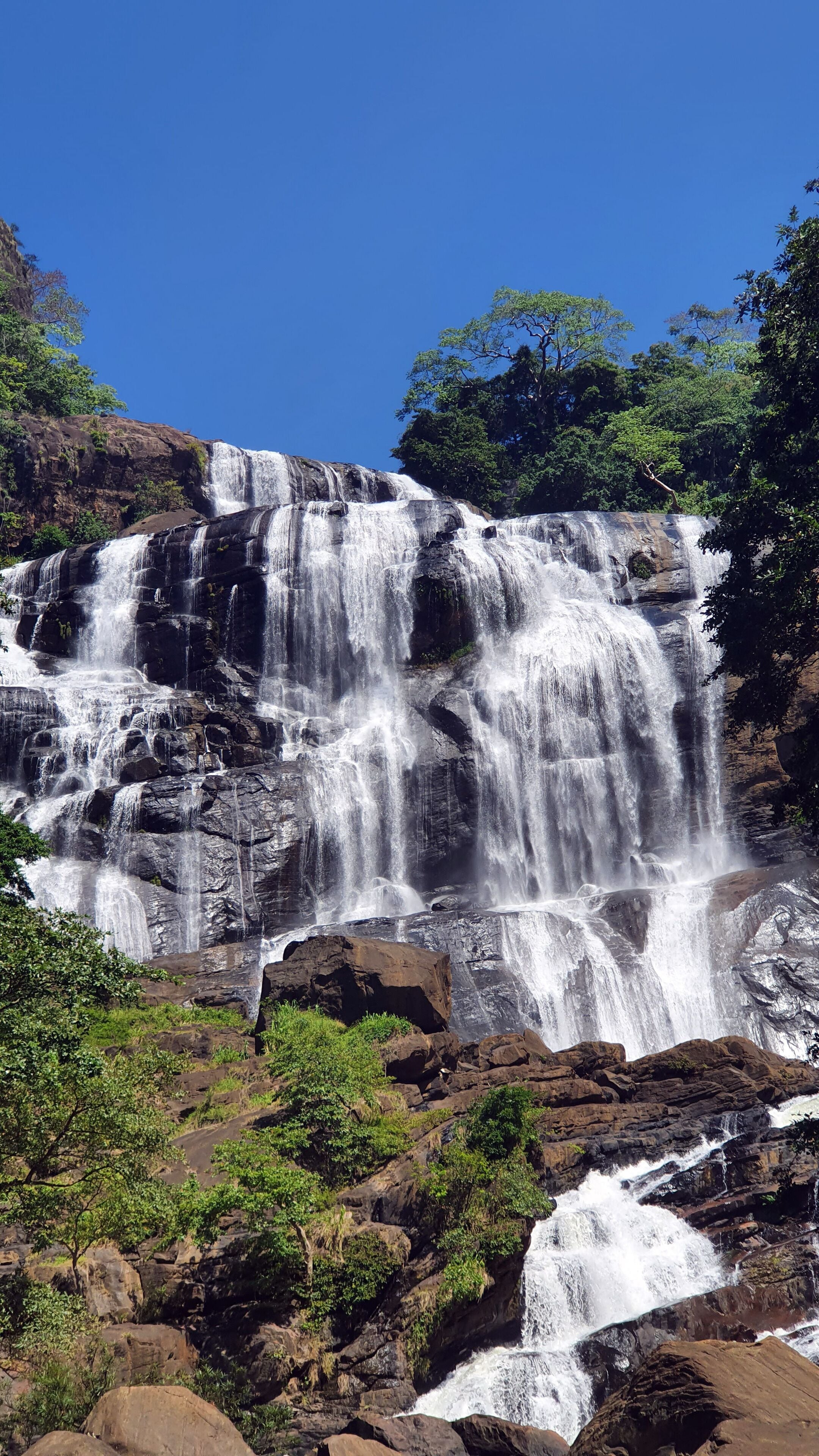 A multi-tiered waterfall surrounded by rocky terrain and lush greenery.