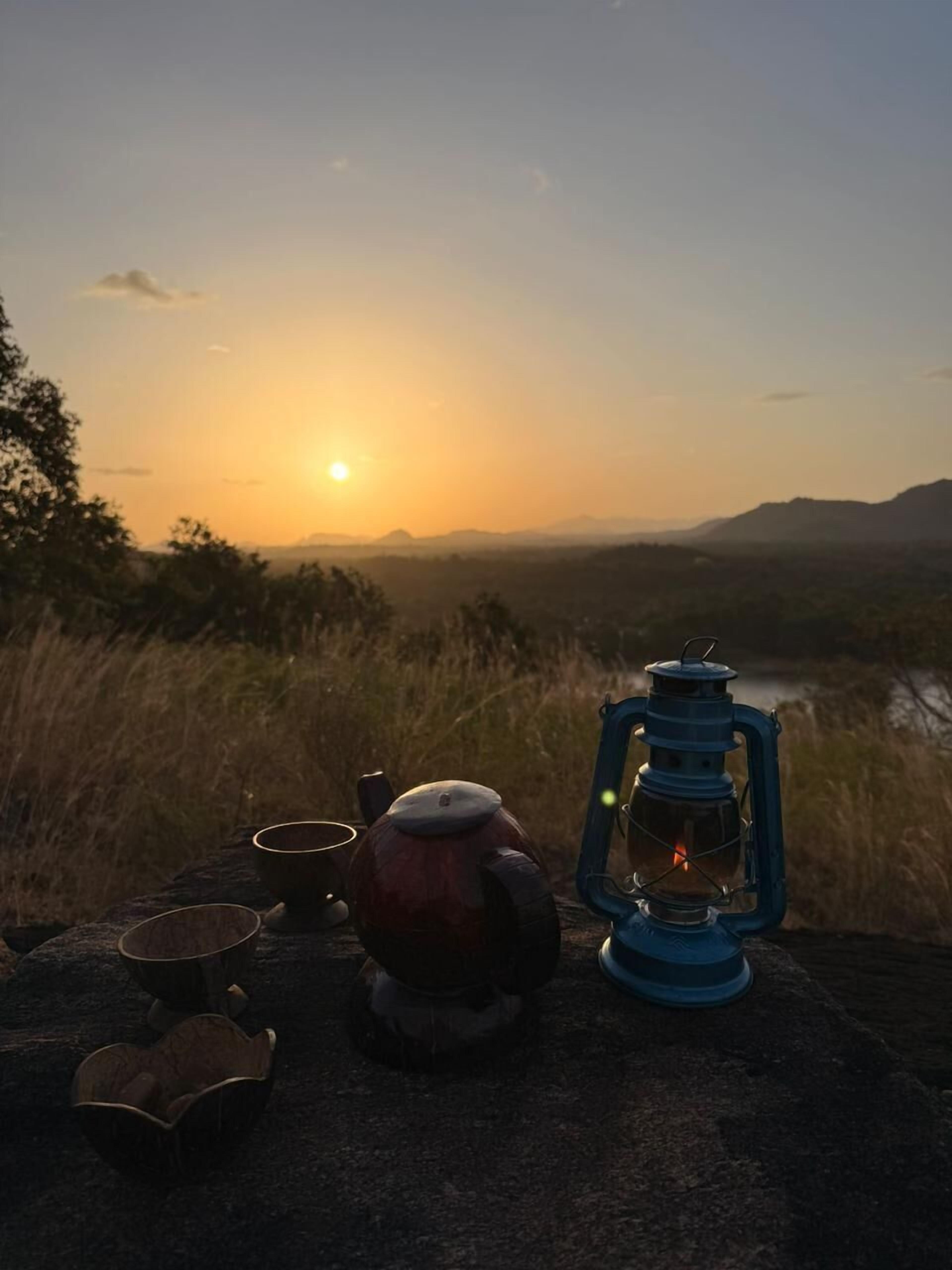 Une vue sur le coucher de soleil, avec une lanterne et une bouilloire posées sur un rocher.