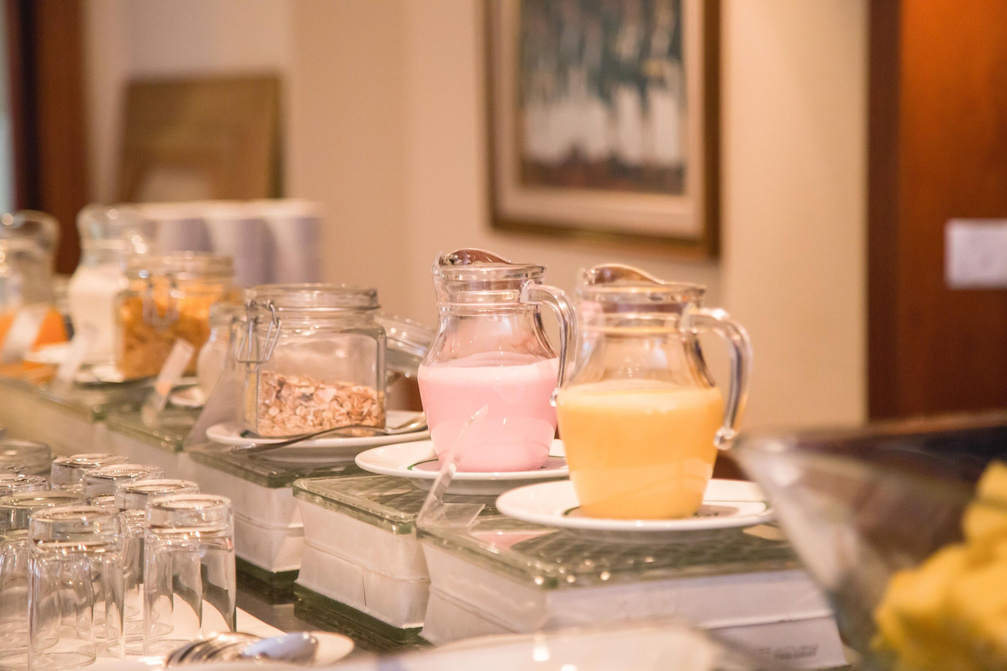 A buffet with various food items and beverages, including a pink smoothie, a yellow smoothie, and a pitcher of orange juice.