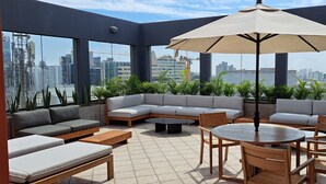A rooftop terrace with a grey sectional sofa, a round wooden table with chairs, and a large umbrella. - Los Tallanes Hotel & Suites (Lima)