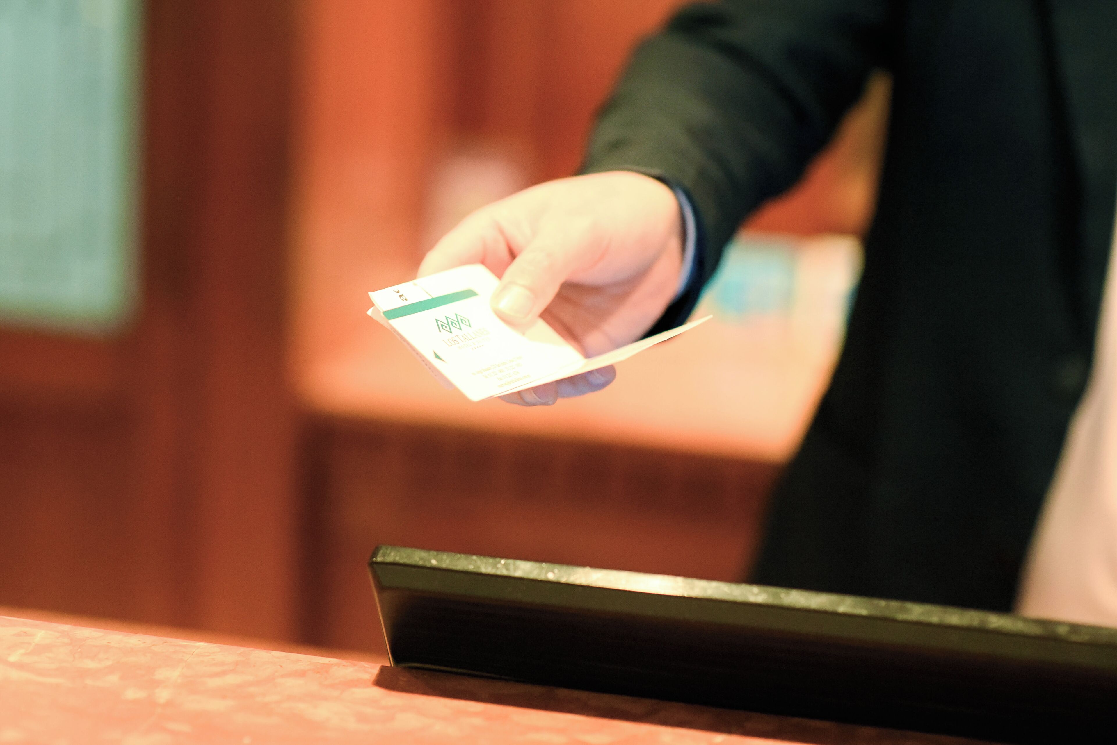 Eine Hand hält eine Karte, vermutlich für den Hotelcheck-in oder die Anmeldung, mit unscharfem Hintergrund, der einen Innenbereich andeutet.