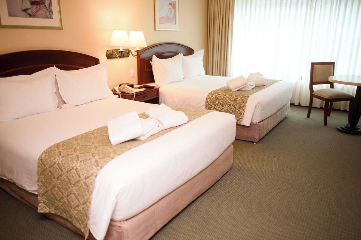 A hotel room with two beds, a chair, and a table.