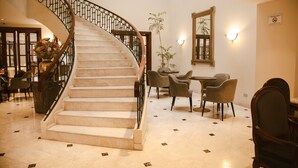 A grand staircase with a metal railing, leading to a dining area with chairs and tables. - Los Tallanes Hotel & Suites (Lima)