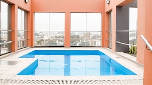 A rooftop swimming pool with clear blue water, surrounded by orange walls and large windows offering city views. - Los Tallanes Hotel & Suites (Lima)