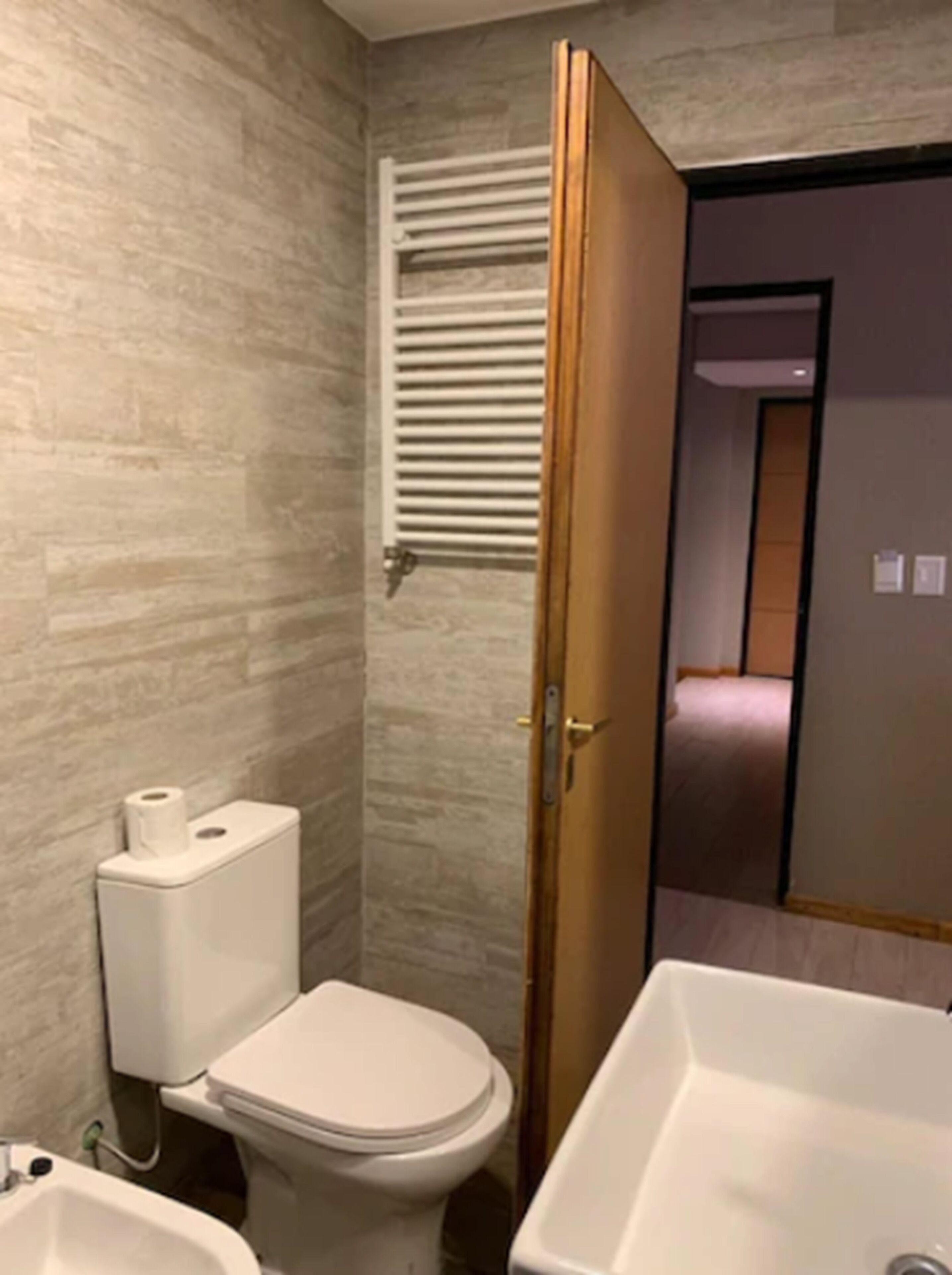 A modern bathroom with a toilet, sink, and a wooden door leading to another room.