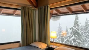 Una habitación con dos camas, vigas de madera en el techo, una ventana con cortinas y una lámpara sobre una mesita de noche.
