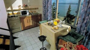 Una cocina compacta con microondas, estufa y armarios, una mesa de comedor con una silla verde, y vista a un lago a través de una ventana.